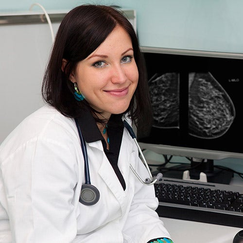 Clinician poses infront of mammography images on computer screen