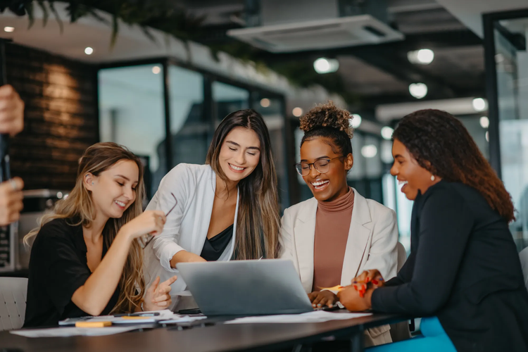 A group of women in an office look at a laptop together