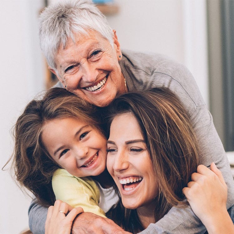 An older woman, younger woman, and young girl share a group hug while smiling at the camera